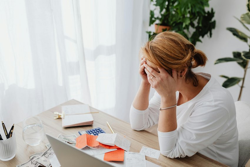 Foto einer Frau am Schreibtisch mit Kopfschmerzen, Kopf in den Händen, Symbolbild für Stress und Migräne im Büro